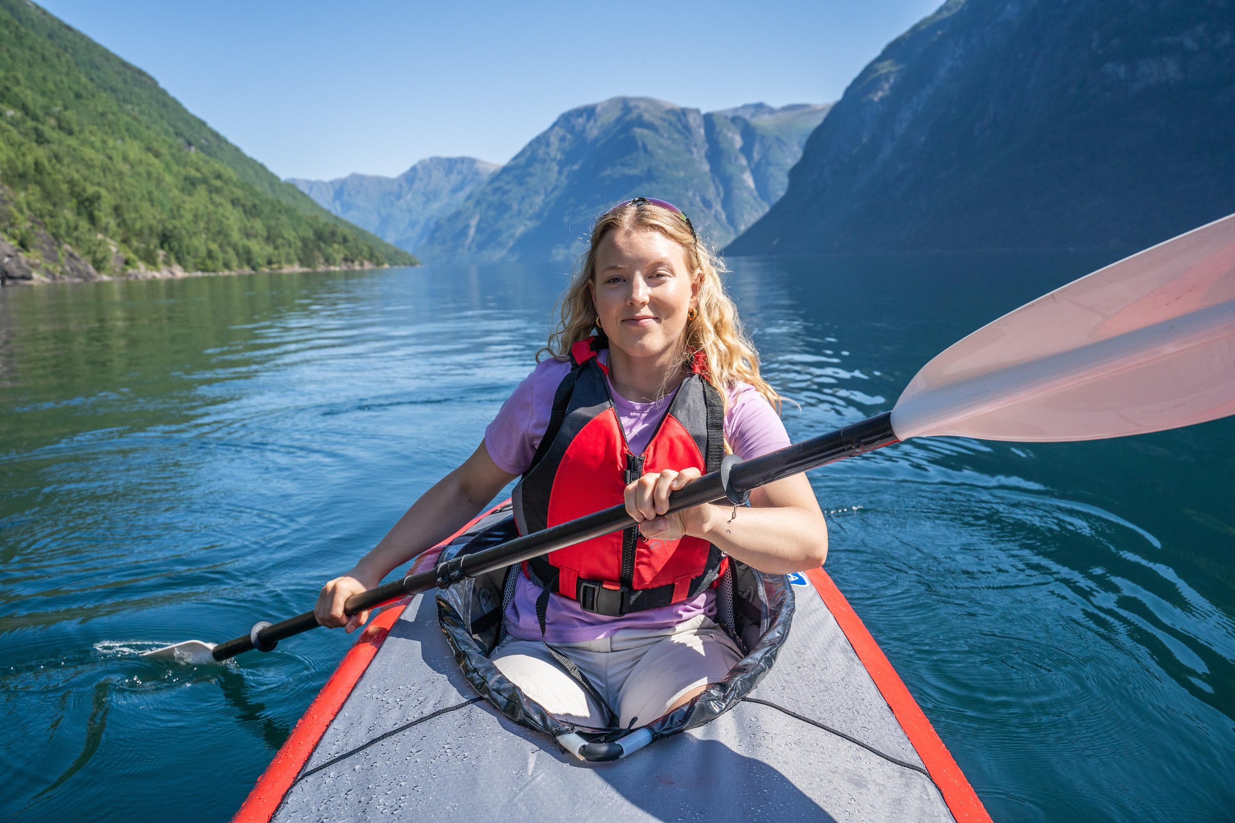Aerial view of kayakers paddling through a crystal-clear Norwegian fjord surrounded by mountains